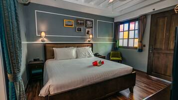 Un dormitorio con una cama grande, mesitas de noche, una silla verde y una ventana con cortinas.