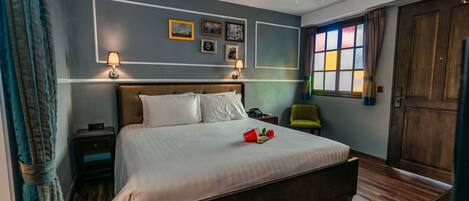 Un dormitorio con una cama grande, mesitas de noche, una silla verde y una ventana con cortinas.