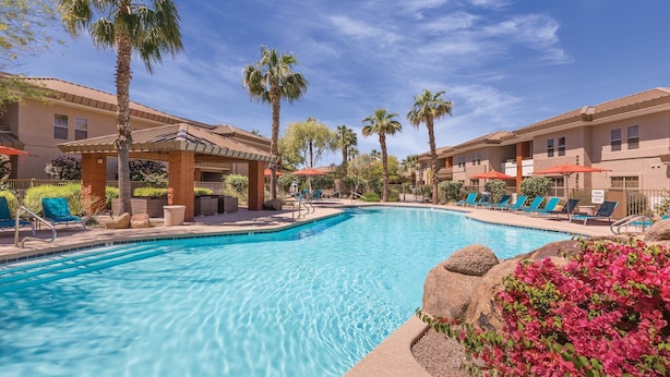 A swimming pool with lounge chairs and palm trees, surrounded by buildings with balconies. - Scottsdale Condo - Great Location, Pool, Full Kitchen (Scottsdale)