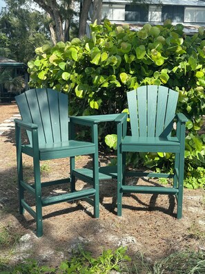 Two green Adirondack chairs with a hedge and trees in the background.