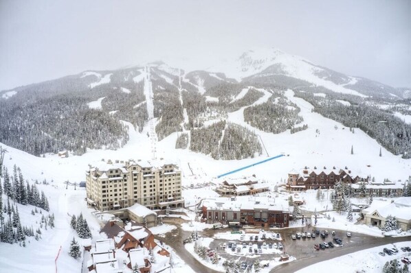 A snow-covered mountain resort with multiple buildings, including a large hotel and smaller structures, surrounded by dense forests and ski slopes.