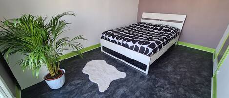 Une chambre à coucher avec un lit, une grande plante en pot et un tapis blanc.