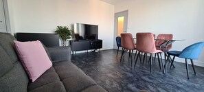 A modern living room with a grey sofa, a TV, a dining table with chairs, and a plant. - 65-square-meter apartment in Paris ♡ Disney ♡ Centrex ☆ RER A (Noisy-le-Grand)
