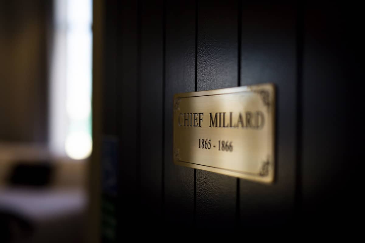Eine Gedenktafel an einer Wand mit dem Namen „CHIEF MILLARD“ und den Jahreszahlen „1865-1866“.