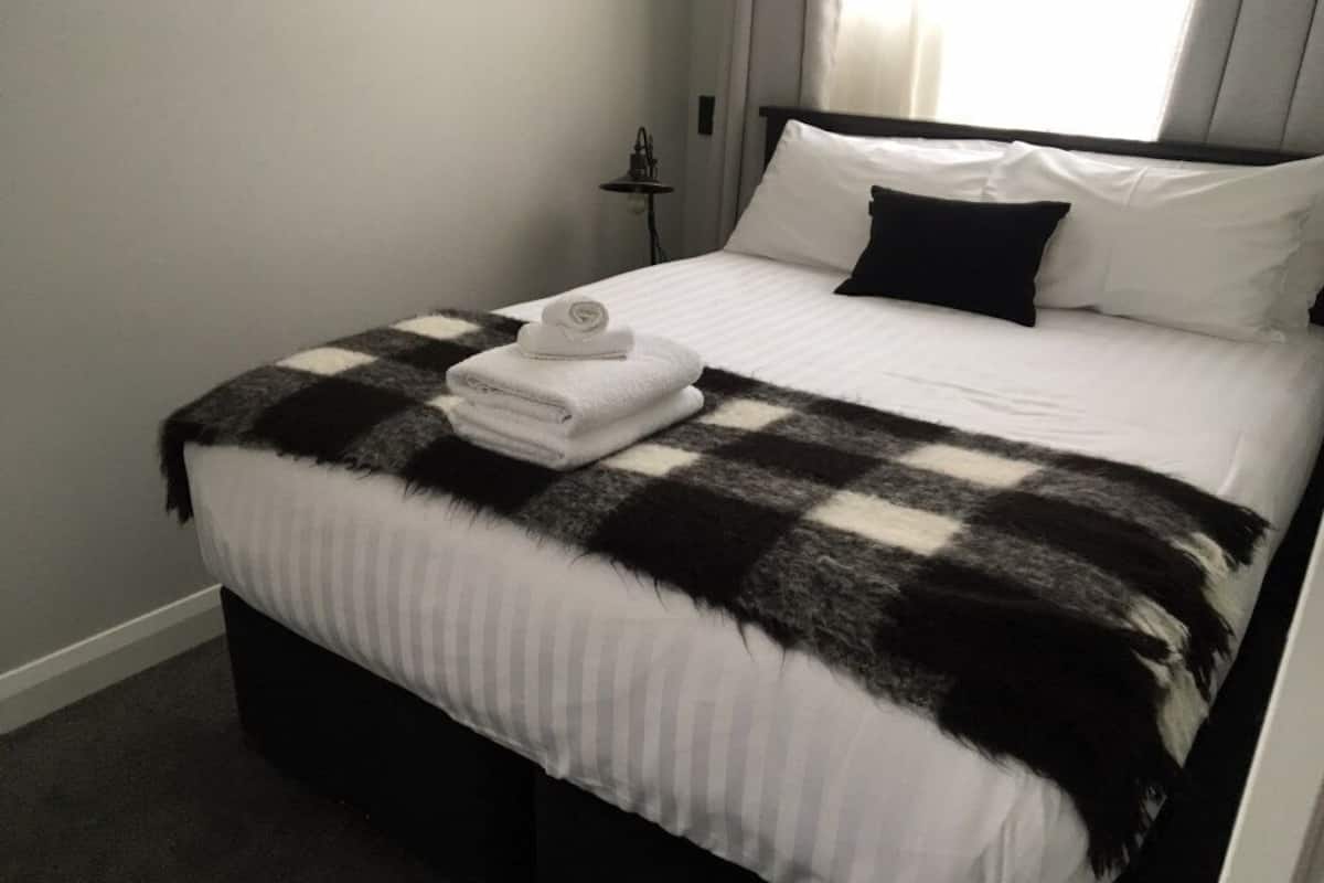 Ein ordentlich bezogenes Bett mit einer karierten Decke, weißen Kissen und gefalteten Handtüchern.