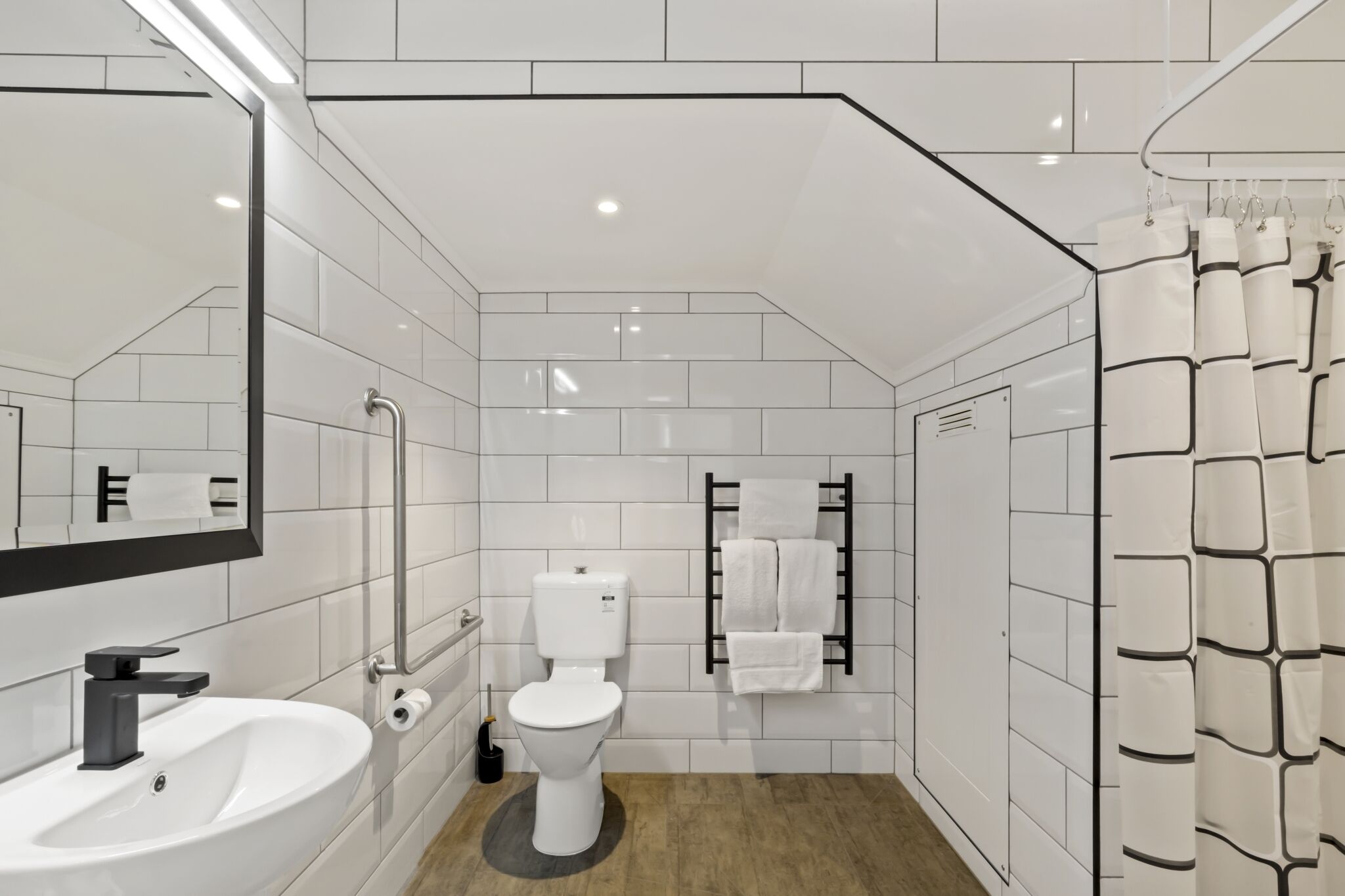 Une salle de bain moderne avec des carreaux blancs, un lavabo, des toilettes, un porte-serviettes et un rideau de douche.
