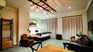 A modern hotel room with a large bed, a wooden dining table, a leather sofa, and a ceiling light fixture. - Hokitika Fire Station Boutique Accommodation (Hokitika)