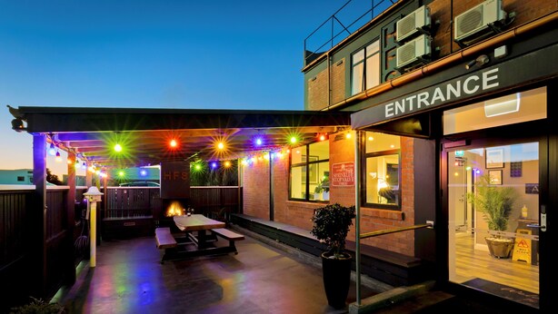 An outdoor patio area with string lights, a wooden deck, and a brick building entrance. - Hokitika Fire Station Boutique Accommodation (Hokitika)