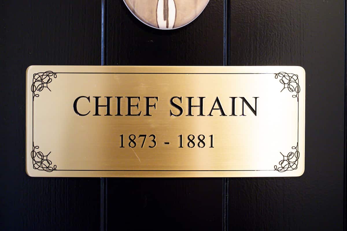 Eine Messingschild mit dem Namen "CHIEF SHAIN" und den Jahreszahlen "1873 - 1881" an einer schwarzen Tür.