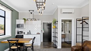 A modern kitchen with white cabinets, a microwave, and a coffee machine. There is a dining table with chairs and a hanging light fixture. - Hokitika Fire Station Boutique Accommodation (Hokitika)