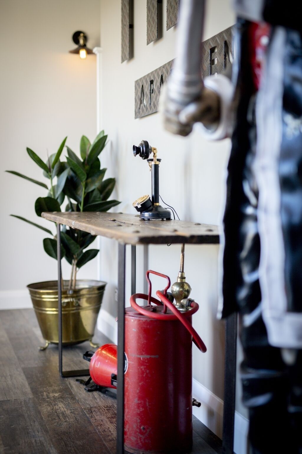 A room with a wooden table, a red gas cylinder, a brass pot, and a potted plant.