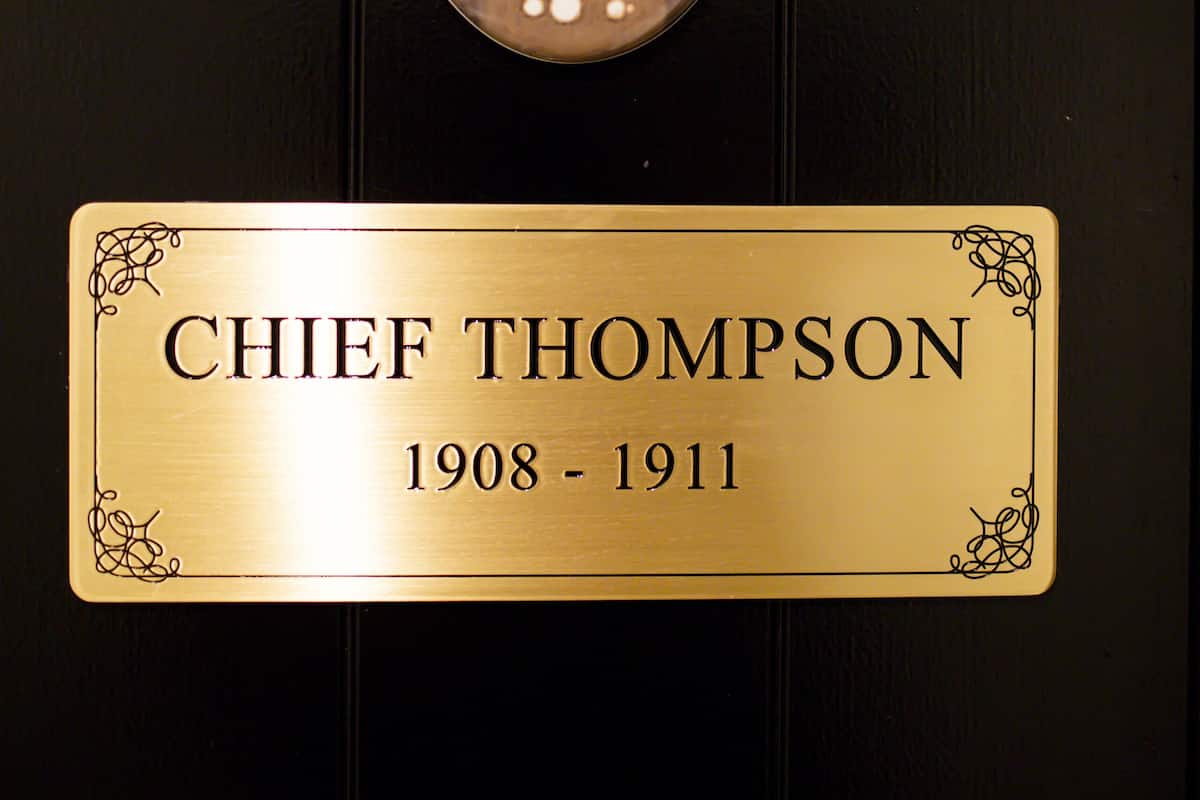 Eine Tafel mit dem Namen "CHIEF THOMPSON" und den Jahreszahlen "1908 - 1911" an einer schwarzen Tür.