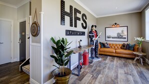 A living room with a brown leather sofa, a wooden coffee table, and a large HFS sign on the wall. - Hokitika Fire Station Boutique Accommodation (Hokitika)