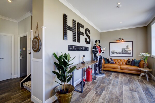 A living room with a brown leather sofa, a wooden coffee table, and a large HFS sign on the wall.