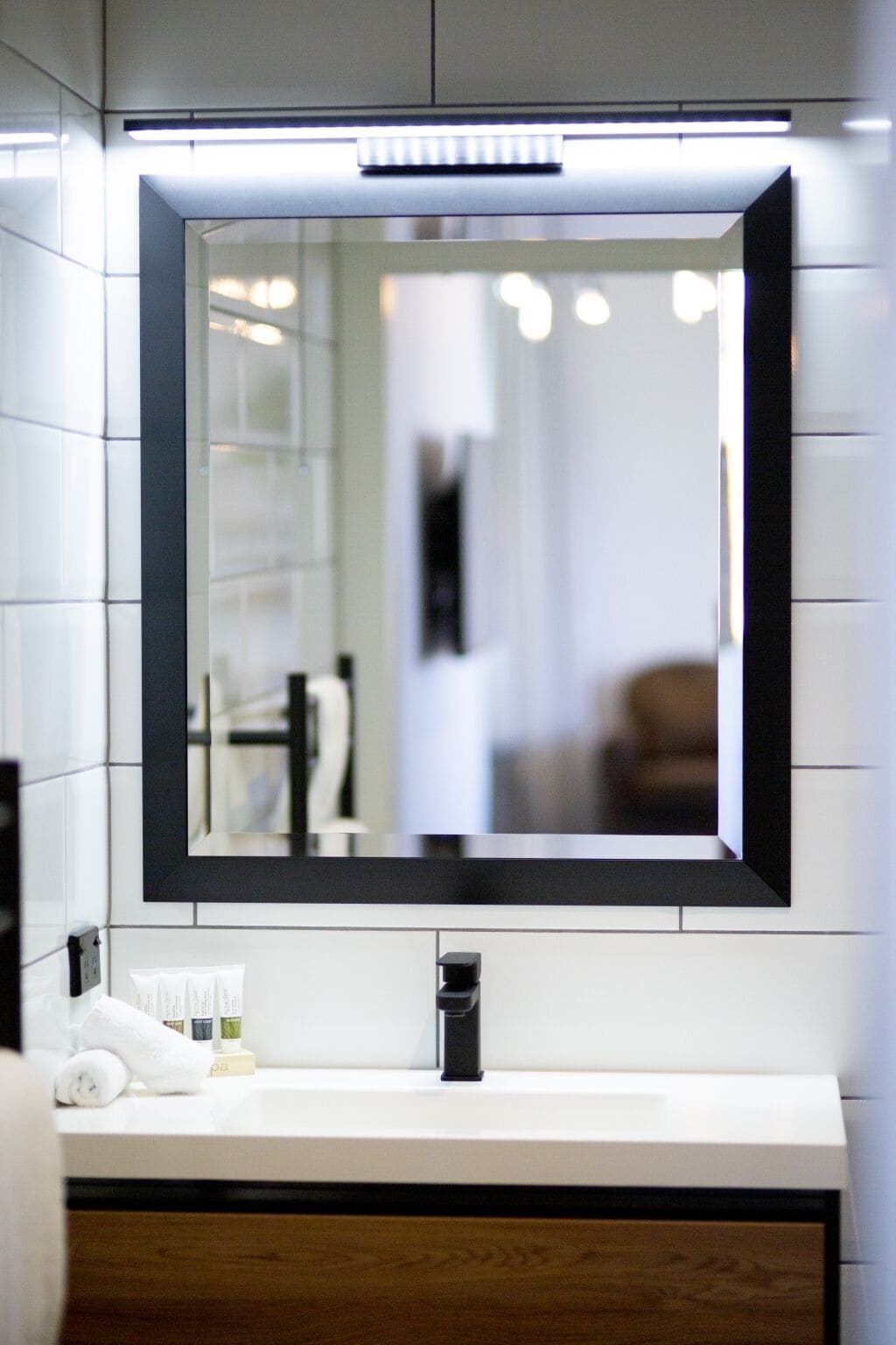 Un baño moderno con un espejo grande, azulejos blancos y un tocador de madera.