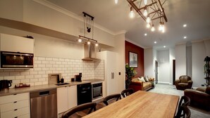 A modern kitchen with a wooden dining table, stainless steel appliances, and a hanging light fixture. - Hokitika Fire Station Boutique Accommodation (Hokitika)