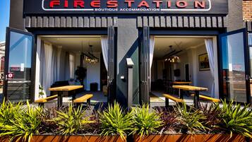 A boutique accommodation named 'Fire Station' with a modern design, featuring a glass entrance, outdoor seating, and potted plants.