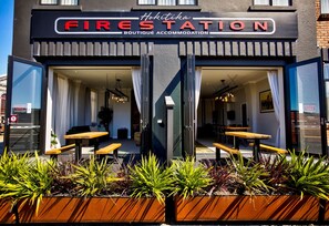 Un alojamiento boutique llamado 'Fire Station' con un diseño moderno, que cuenta con una entrada de cristal, asientos exteriores y plantas en macetas.