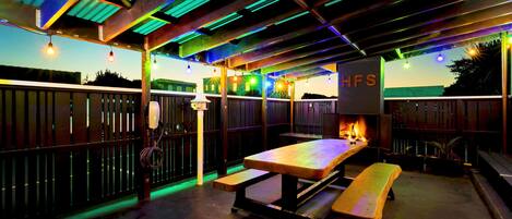 Ein möblierter Terrassenbereich mit Holztisch und -bänken, einem Grill und Lichterketten.