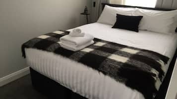 A neatly made bed with a checkered blanket, white pillows, and folded towels on the side.