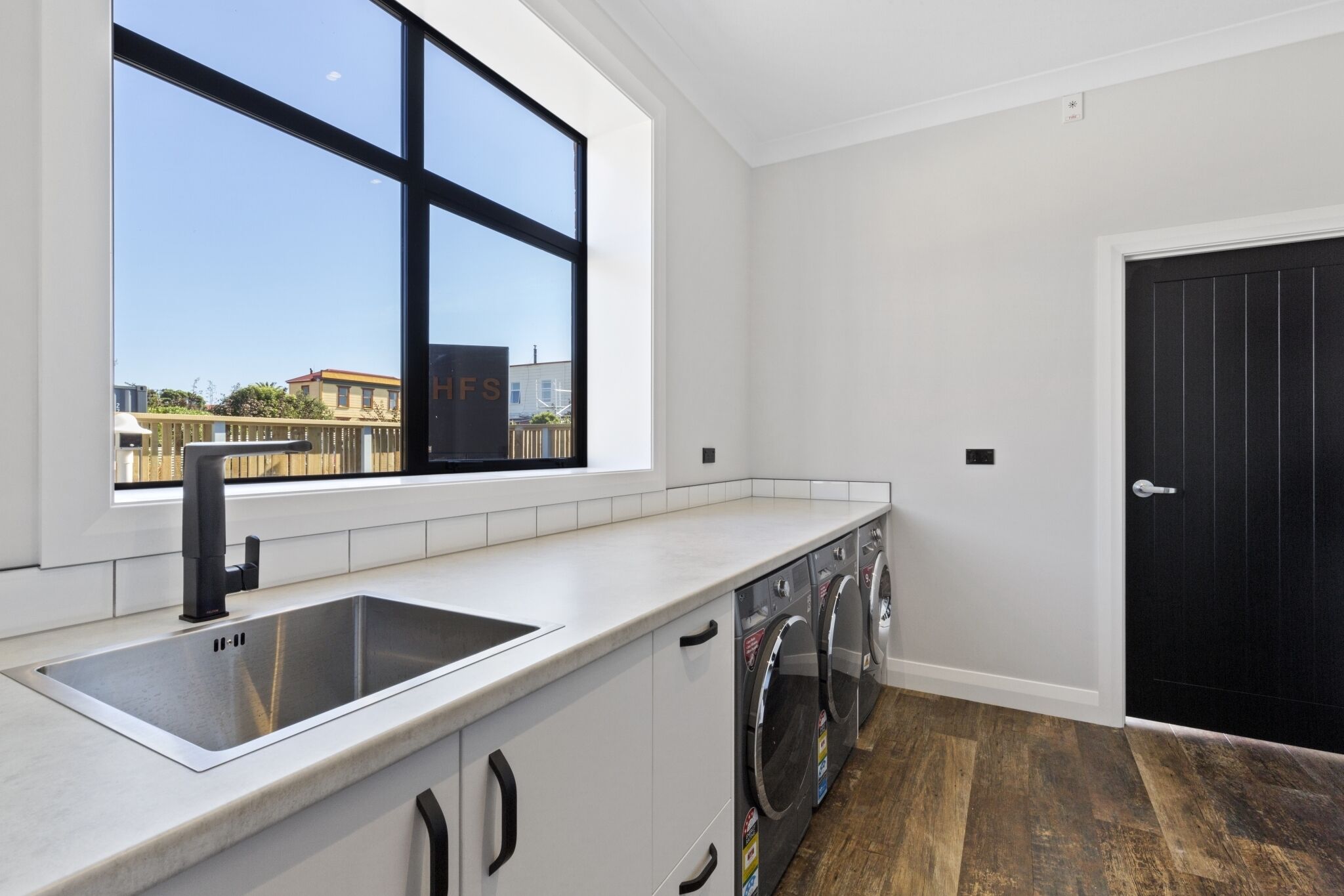 A modern kitchen with a large window, a stainless steel sink, and a black door.