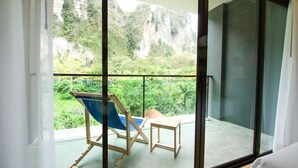 Un balcón con vistas a un paisaje verde exuberante y acantilados. Hay una silla de madera y una mesita en el balcón.