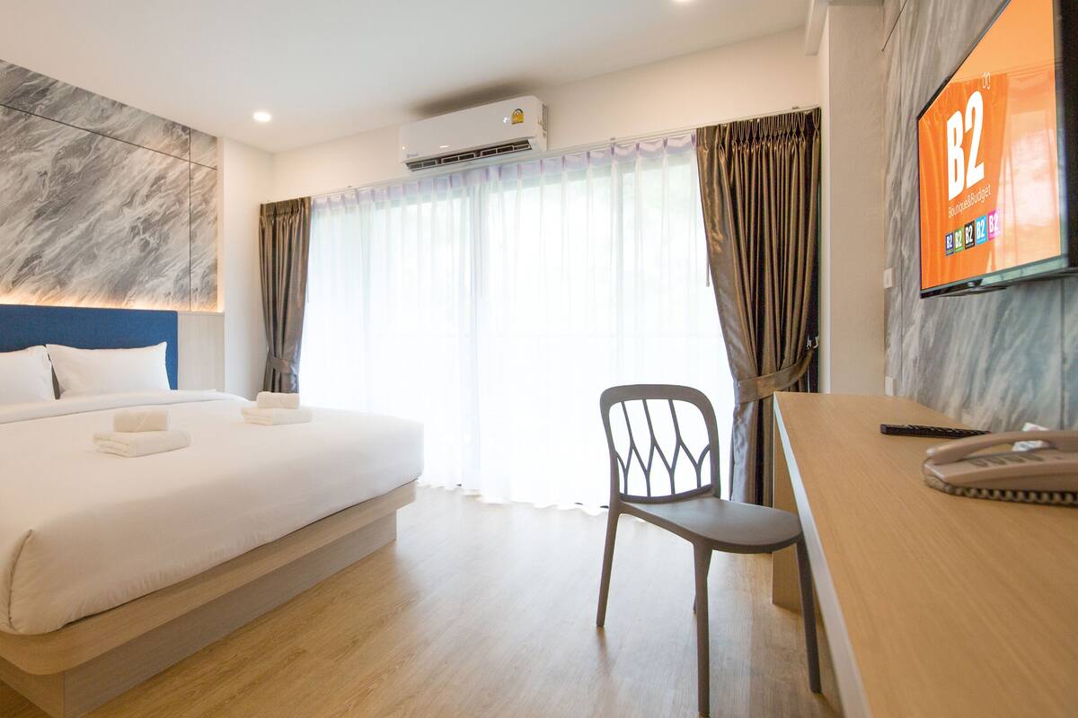 Habitación de hotel con una cama grande, un escritorio, una silla y un televisor mostrando 'B2 Boutique & Budget'.