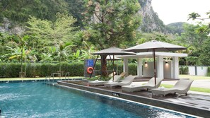 A pool area with lounge chairs and umbrellas, surrounded by lush greenery and a mountainous backdrop. - B2 Krabi Ao Nang Premier Resort (Krabi)
