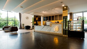 Un moderno vestíbulo de hotel con un mostrador de recepción de mármol, zona de estar y una vitrina con pasteles.