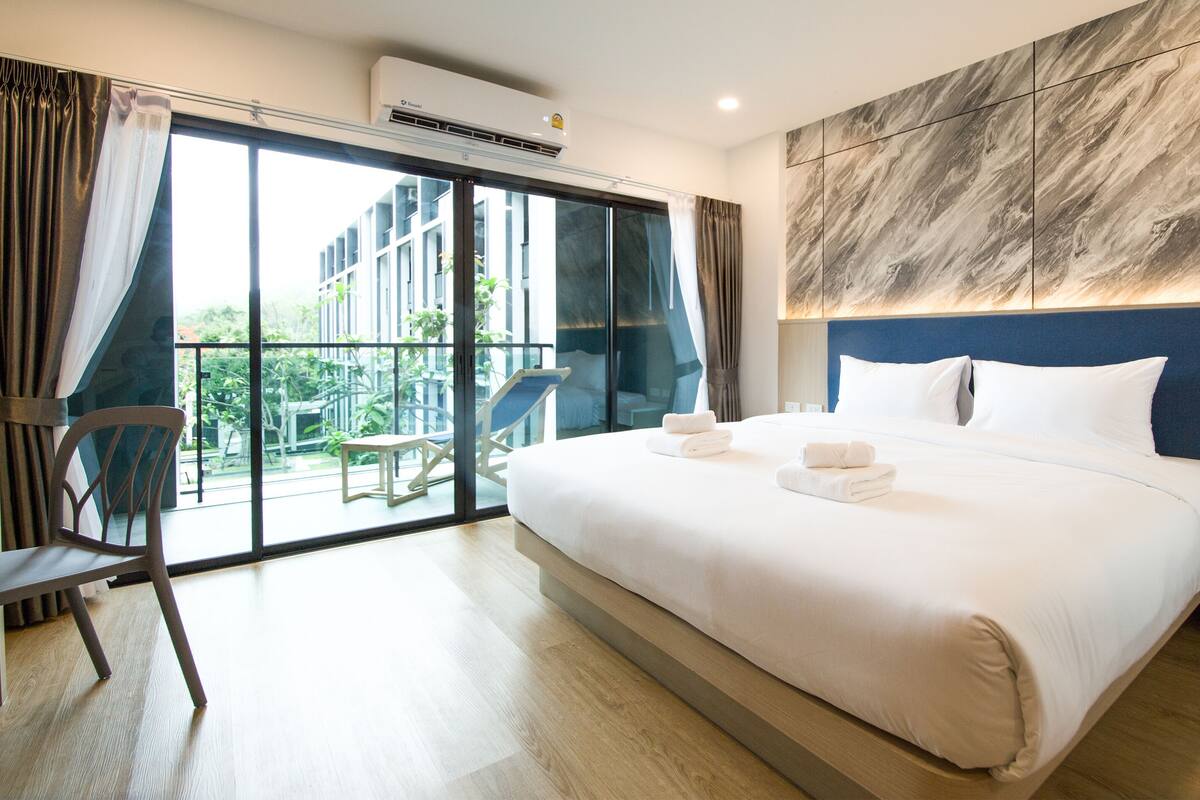Habitación de hotel moderna con una cama grande, un balcón con una silla y vistas al exterior.