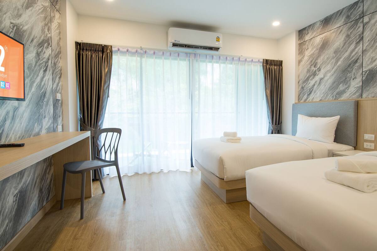 Habitación de hotel con dos camas, un escritorio, una silla, un televisor y un equipo de aire acondicionado.