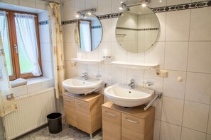 A bathroom with two sinks, a mirror, and a window with curtains. - Apartment (82 m²), balcony, kitchen, 1 bedroom, and 1 living room/bedroom, max. 3 people (Ruhpolding)