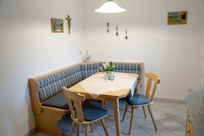 A corner dining area with a wooden bench and chairs, a table with a white tablecloth, and a hanging light fixture. - Apartment (82 m²), balcony, kitchen, 1 bedroom, and 1 living room/bedroom, max. 3 people (Ruhpolding)