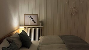 Un dormitorio con cama, almohadas, un cuadro enmarcado, un radiador y un objeto decorativo en la pared.