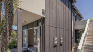 A modern building with a wooden deck, a covered outdoor area, and a staircase. - Golfer's Paradise - Matarangi Holiday Home (Matarangi)