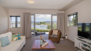 A modern living room with a sofa, a wicker chair, a coffee table, and a TV. - Golfer's Paradise - Matarangi Holiday Home (Matarangi)
