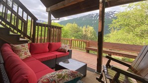 Ein überdachter Sitzbereich im Freien mit einer roten Couch und einem Holztisch, mit Blick auf eine gebirgige Landschaft.