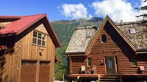 Eine Holzhütte mit rotem Dach, einer Veranda mit Sitzgelegenheit und einem Bergpanorama im Hintergrund.