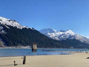 A beach with a wooden structure in the foreground, a clear blue sky, and snow-capped mountains in the background.
