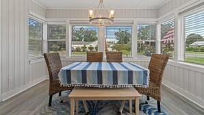 A dining area with a table and chairs, a chandelier, and large windows with blinds.
