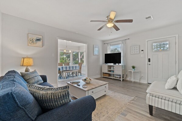 A living room with a sofa, coffee table, TV, and a ceiling fan. - 2 bedrooms - King bed - close to beaches - beautiful deck with outdoor seating. (Pensacola)