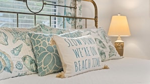 A bed with decorative pillows featuring sea creature prints and a text pillow saying "SLOW DOWN WE'RE ON BEACH TIME".