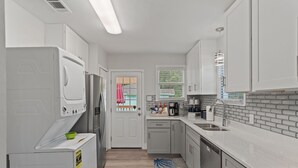 A modern kitchen with white appliances, grey cabinets, and a window with blinds.