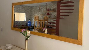 Een spiegel met houten lijst toont een keukenhoek met een houten stoel, een vaas met bloemen en een betegelde achterwand.