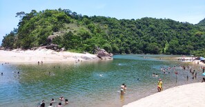 A beach with people swimming and sunbathing, surrounded by lush greenery and rocky outcrops. - Beach House, Sapê - Maranduba, on a dead-end street—peaceful and with beautiful scenery! (Ubatuba)