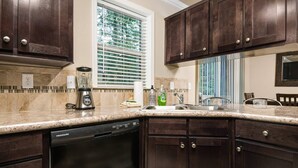A kitchen with dark wood cabinets, a granite countertop, a dishwasher, and a window with blinds. - Newly Constructed, Single Level, Open Layout, Walk to Sandy River, 17 Miles to Government Camp (Rhododendron)