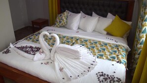 A neatly made bed with a geometric patterned bedspread, a headboard, and a small bedside table. - The Hydeout Riviera (Kisumu)
