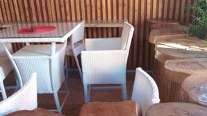 A wooden outdoor seating area with wicker chairs and round wooden tables. - The Hydeout Riviera (Kisumu)