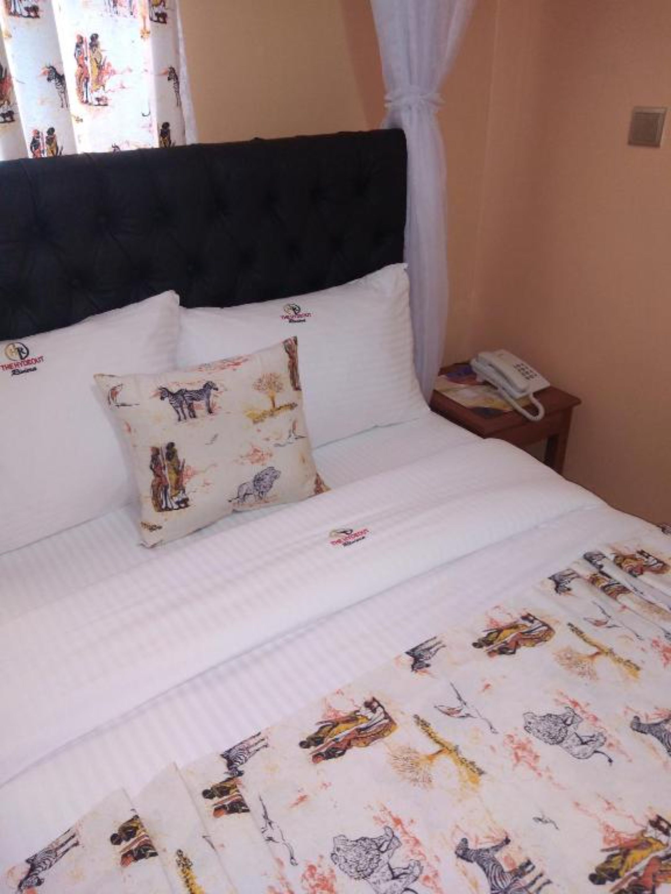 A bed with a white bedspread featuring animal prints, a black headboard, and a single decorative pillow with a similar print.