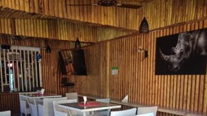 A restaurant with wooden walls and ceiling, white wicker furniture, and a bull-themed painting. - The Hydeout Riviera (Kisumu)
